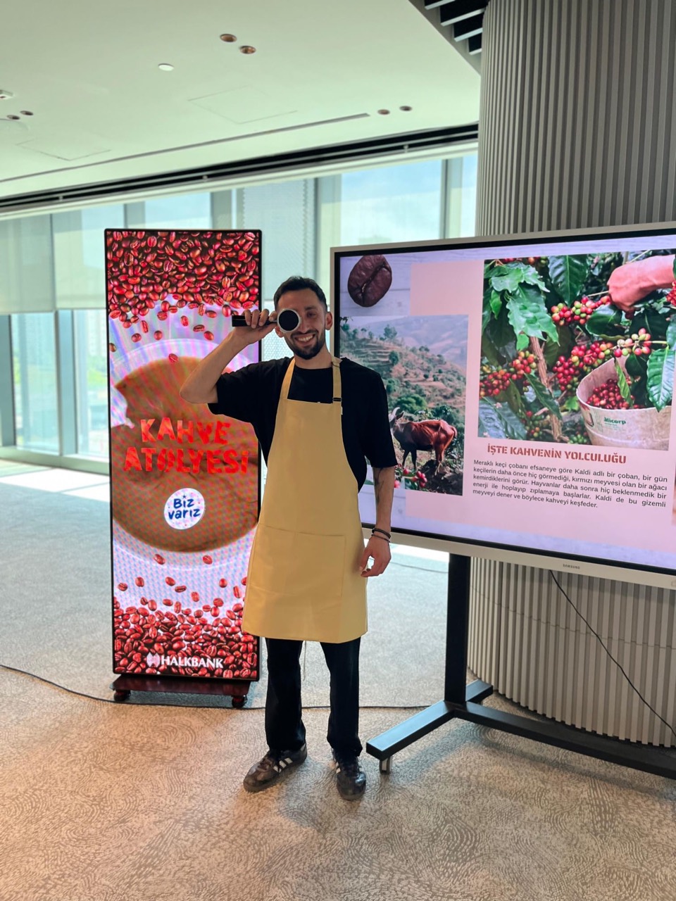 A person wearing an apron and holding a portafilter beside coffee presentation screens
